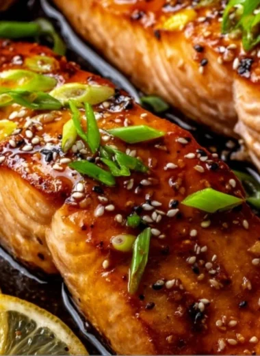 A plate of baked teriyaki salmon garnished with green onions and sesame seeds