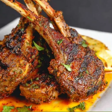 Juicy oven-baked lamb chops garnished with herbs on a serving plate.