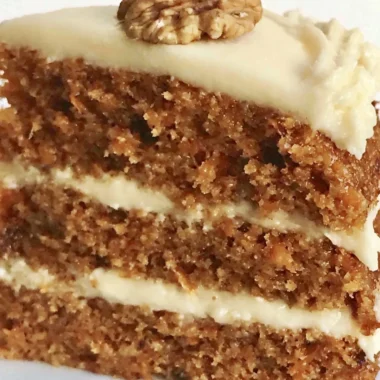 Slice of classic carrot cake with cream cheese frosting on a white plate.