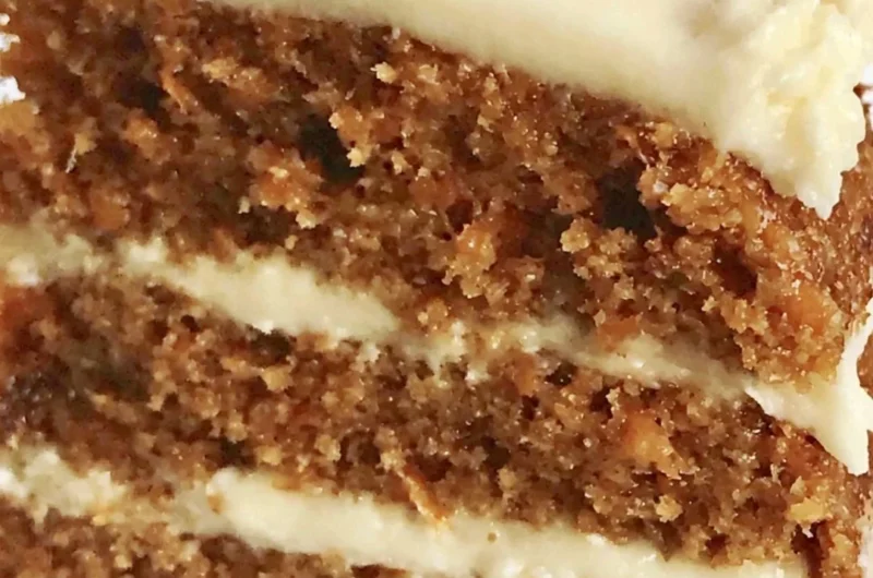 Slice of classic carrot cake with cream cheese frosting on a white plate.