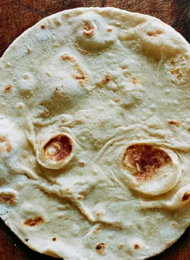 Homemade sourdough tortillas stacked on a wooden board with fresh ingredients